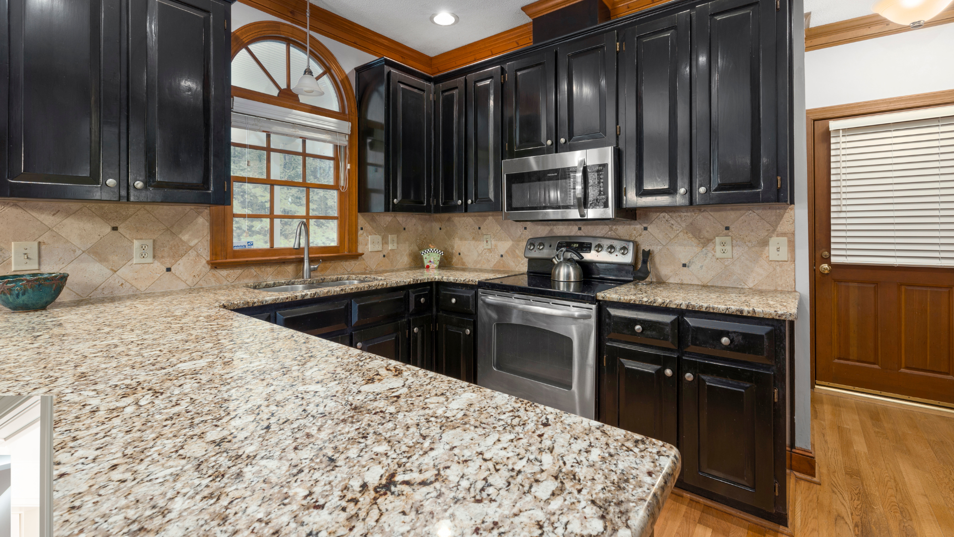 A kitchen with granite counter tops , black cabinets and stainless steel appliances.
