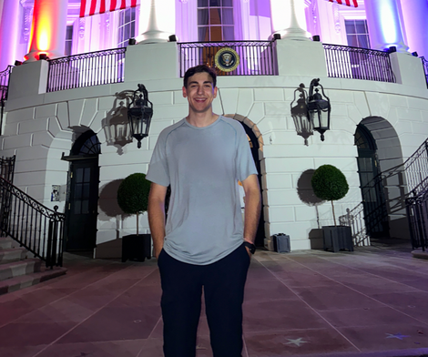 Man standing in front of the White House at night, arms in pockets, smiling.