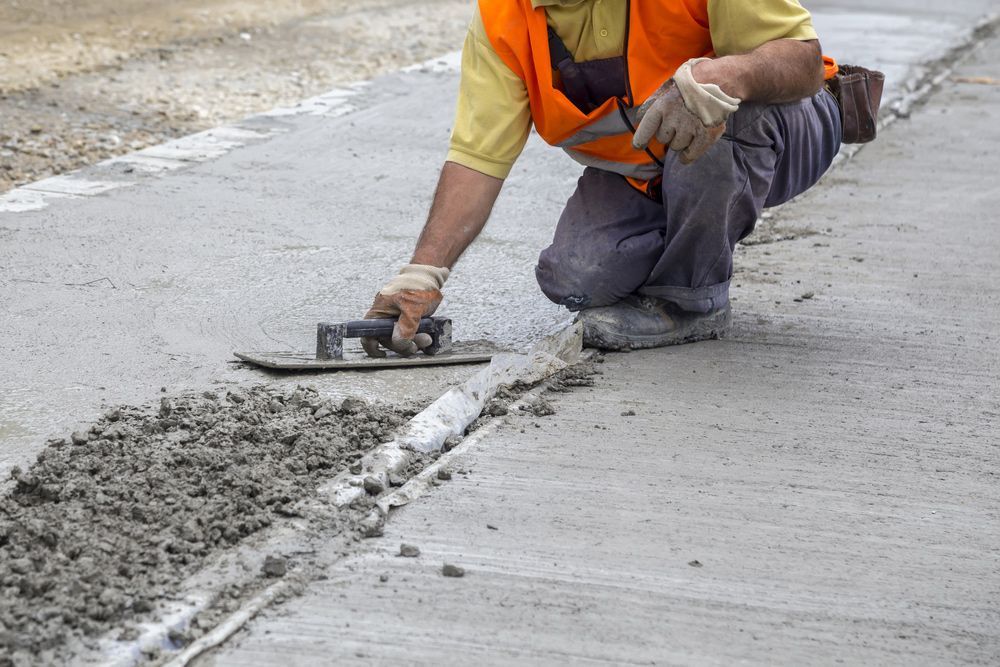 A man is kneeling down and spreading concrete on a sidewalk.