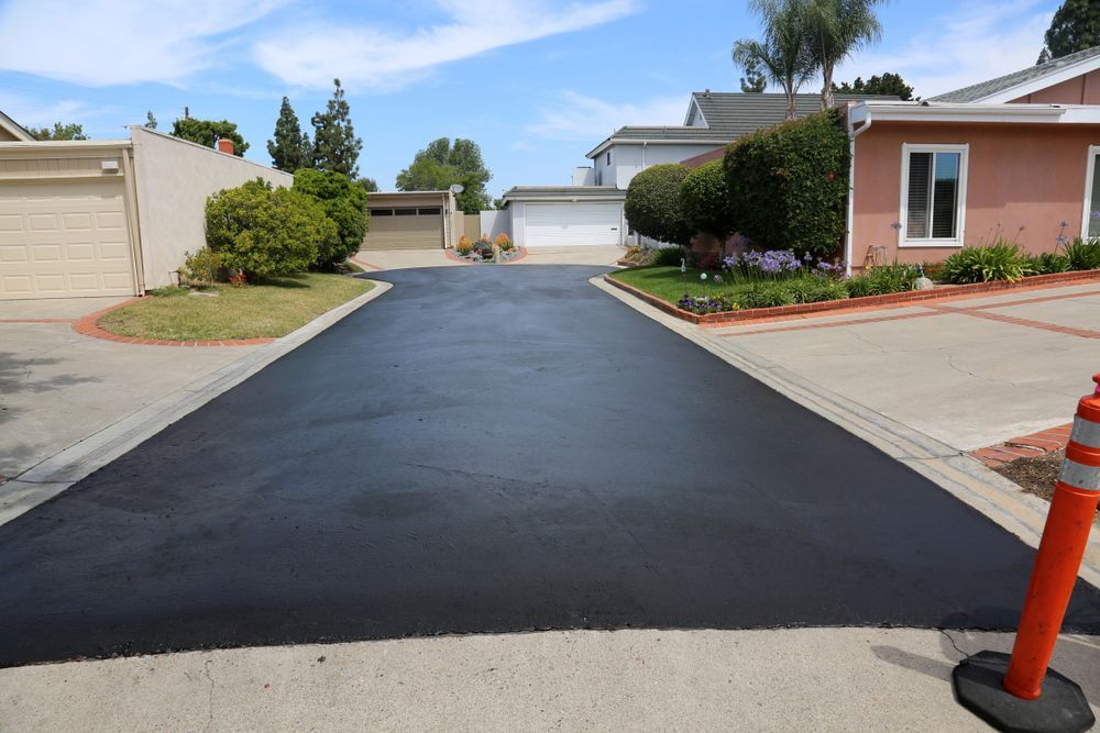 A newly paved driveway in a residential neighborhood with a pink house in the background.