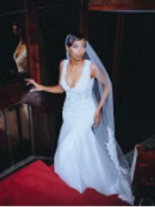 Bride in a white gown and veil stands on a red staircase, looking to the side.