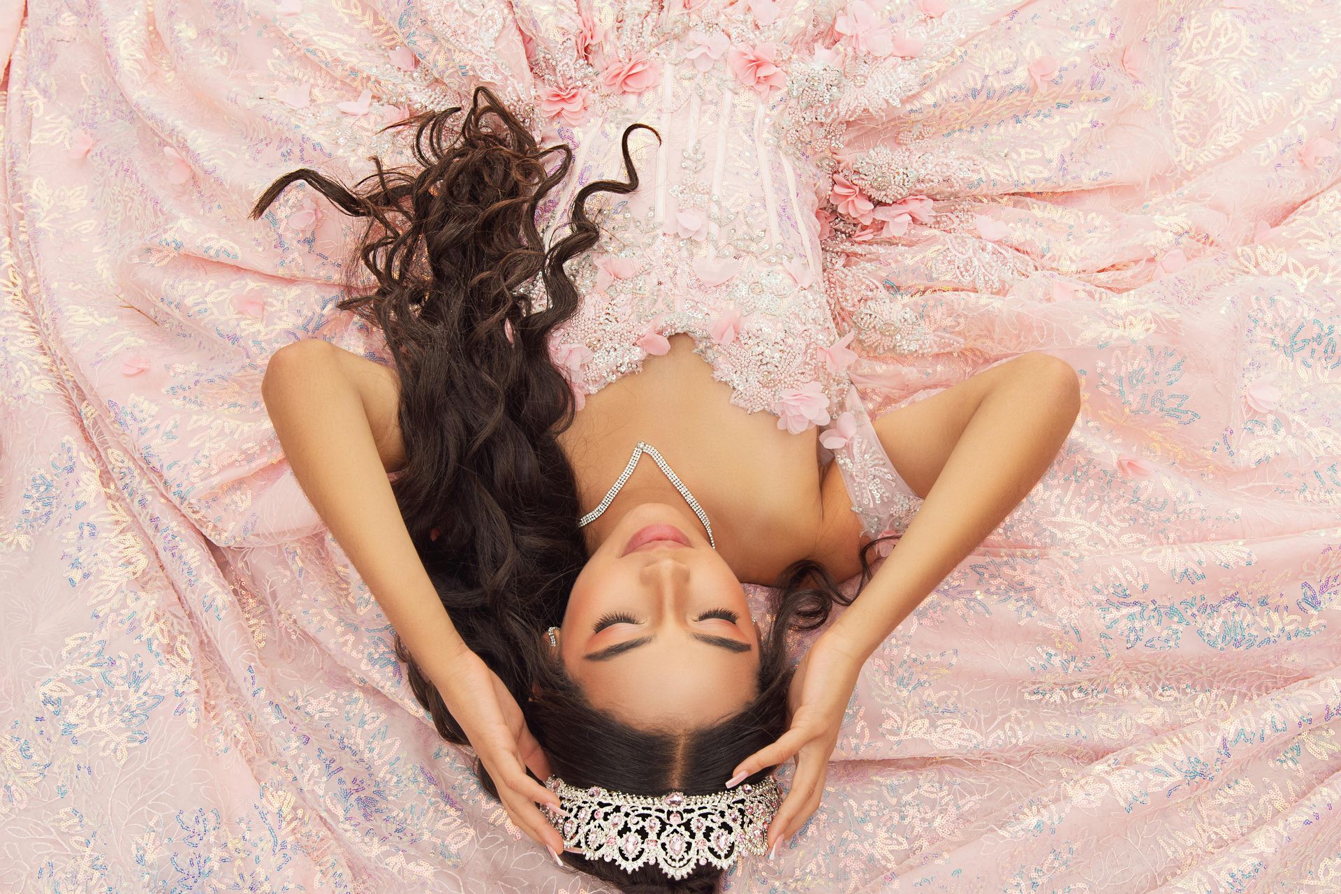 Woman smiling, looking at formal dresses in a store. She is wearing a beaded, rose-colored dress.
