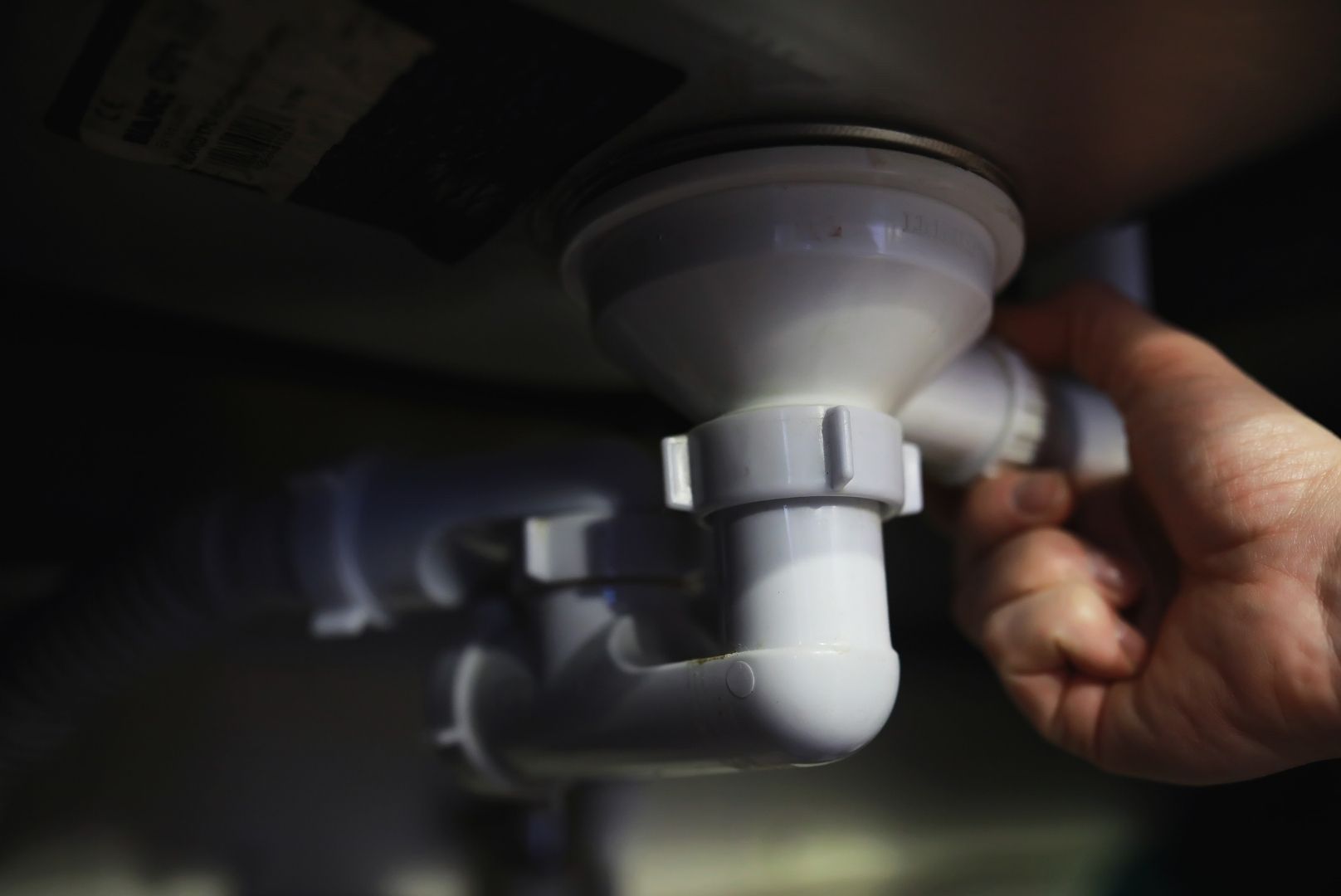 A person is fixing a sink drain with their hand