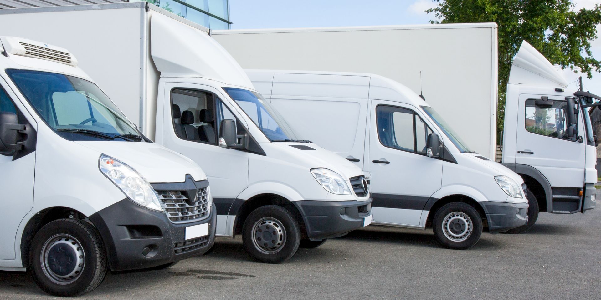 Three white vans are parked next to each other in a parking lot.