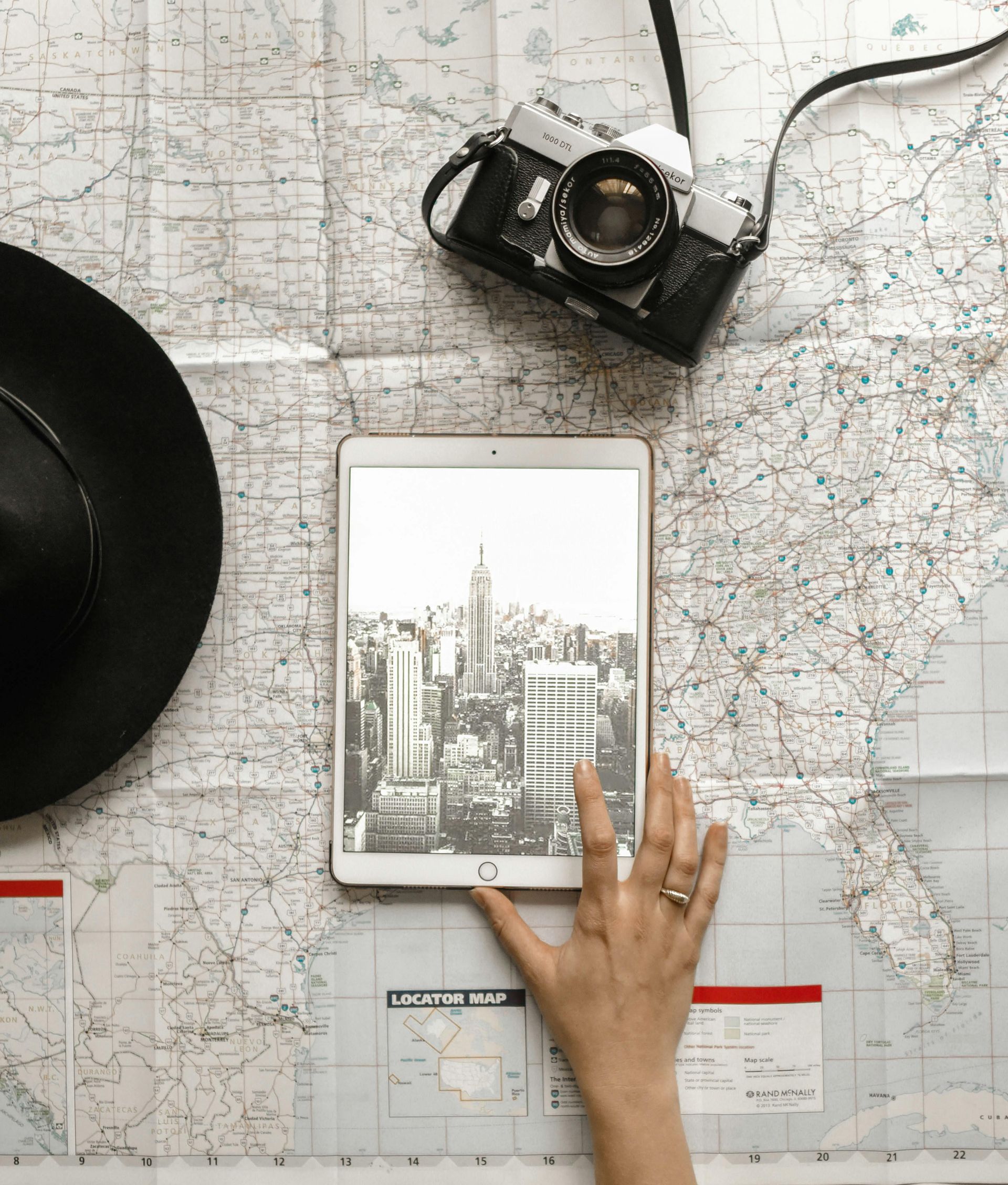 Hand holding a tablet displaying a city skyline on a map with a camera and hat.