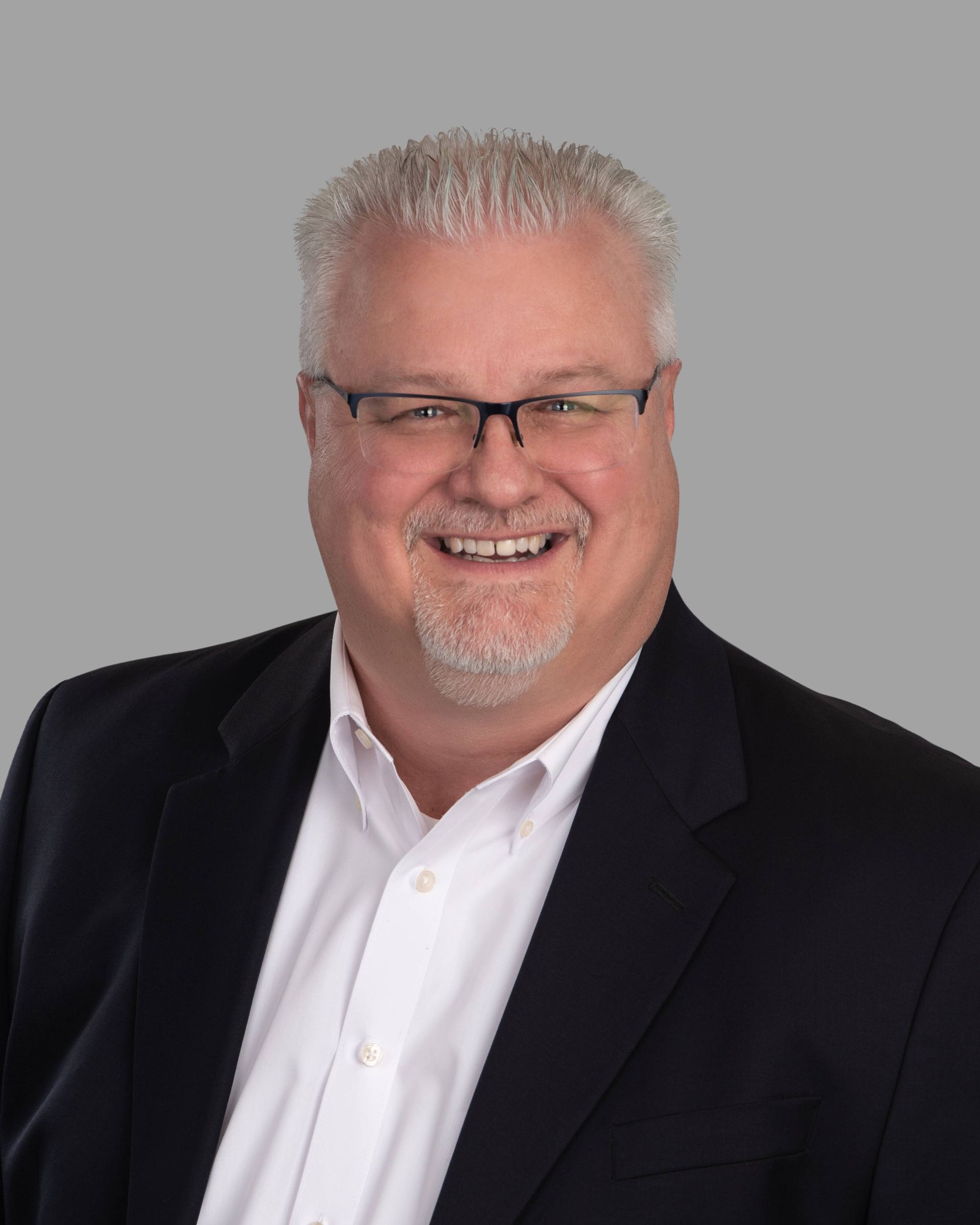 A man wearing a suit and glasses is smiling for the camera.