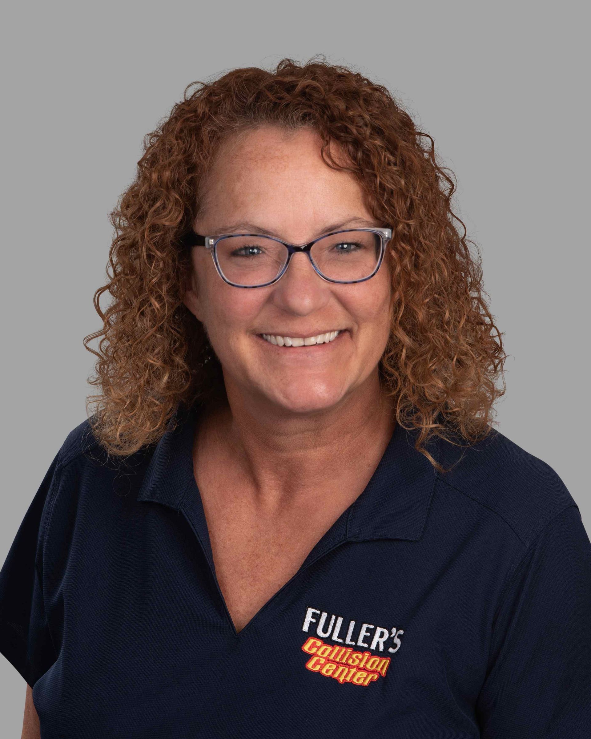 A woman wearing glasses and a blue shirt is smiling for the camera.