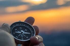 A person is holding a compass in their hand in front of a sunset.