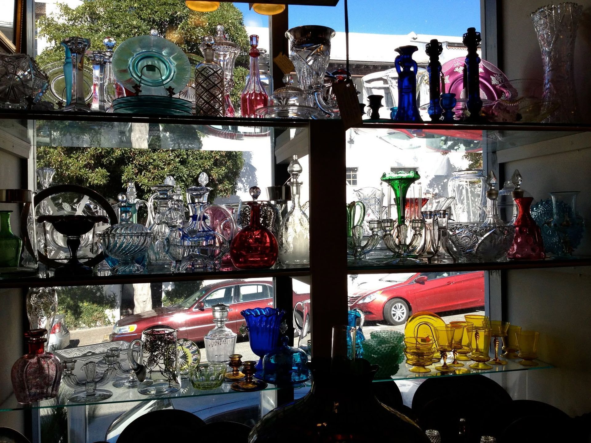 Shelves of colorful glass decorative pieces displayed in a shop window, with cars visible outside