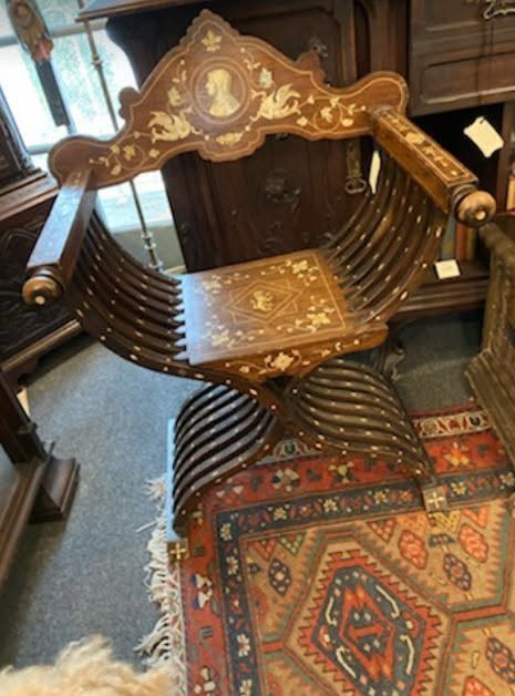 Ornate wooden chair with inlaid details and curved slats on a patterned rug in an antique shop