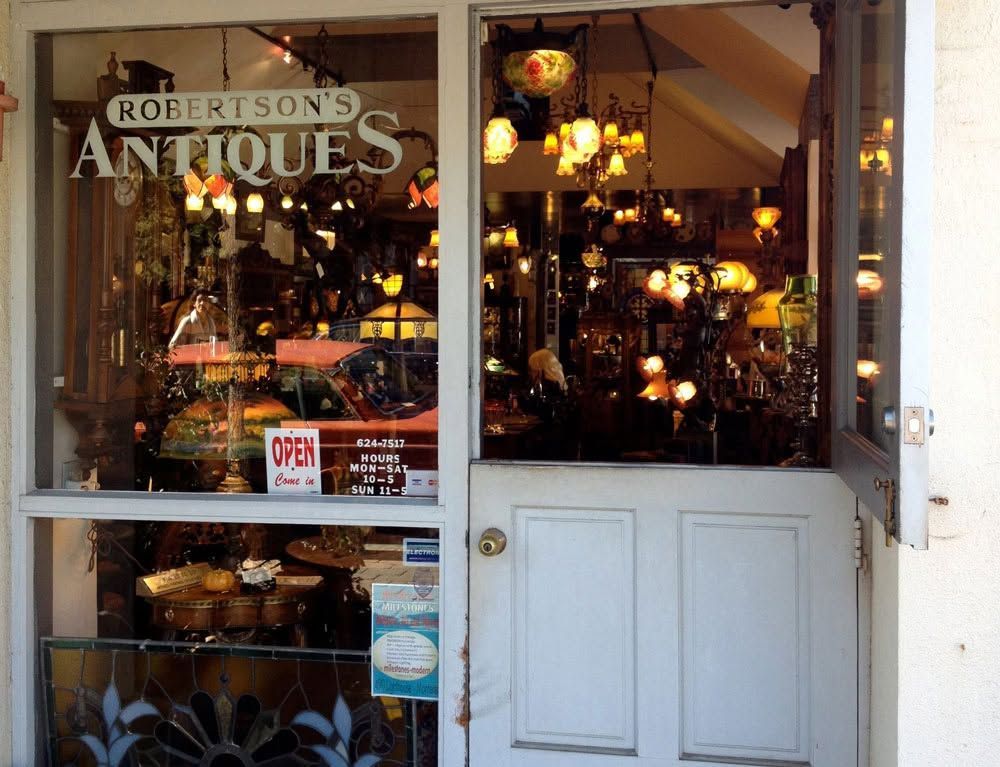 Storefront window of Robertson’s Antiques, lit with hanging lamps and displays inside