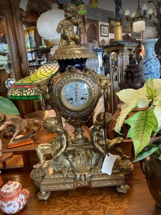 Ornate vintage mantel clock with bronze figures on a carved wooden base in an antique shop.
