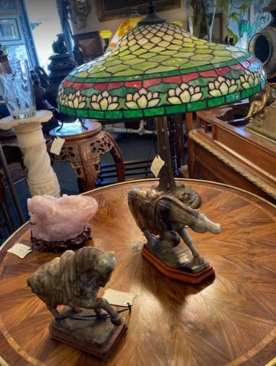 Wooden table with three small animal figurines and a green stained-glass lamp in an antique shop.