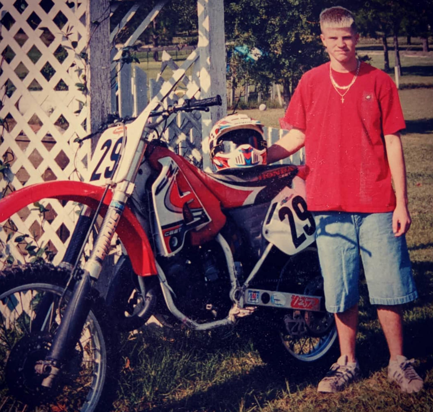 a man in a red shirt stands next to a dirt bike with the number 29 on it