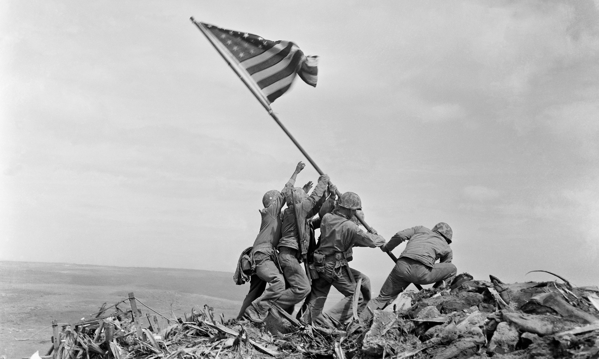 a group of soldiers are raising an american flag on top of a hill .