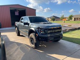 A ford raptor truck is parked in a driveway in front of a garage.