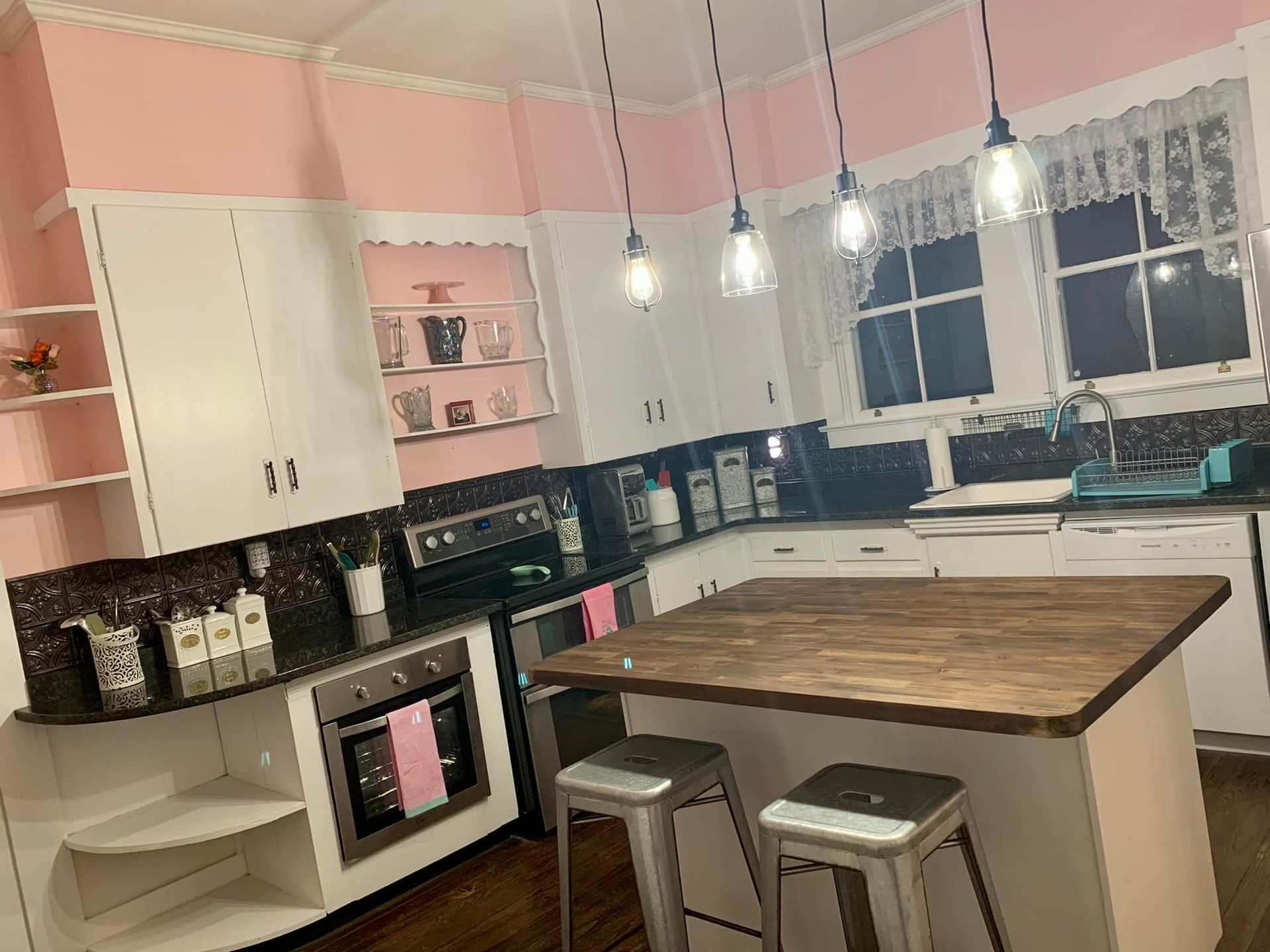 A kitchen with pink walls and white cabinets and a wooden table