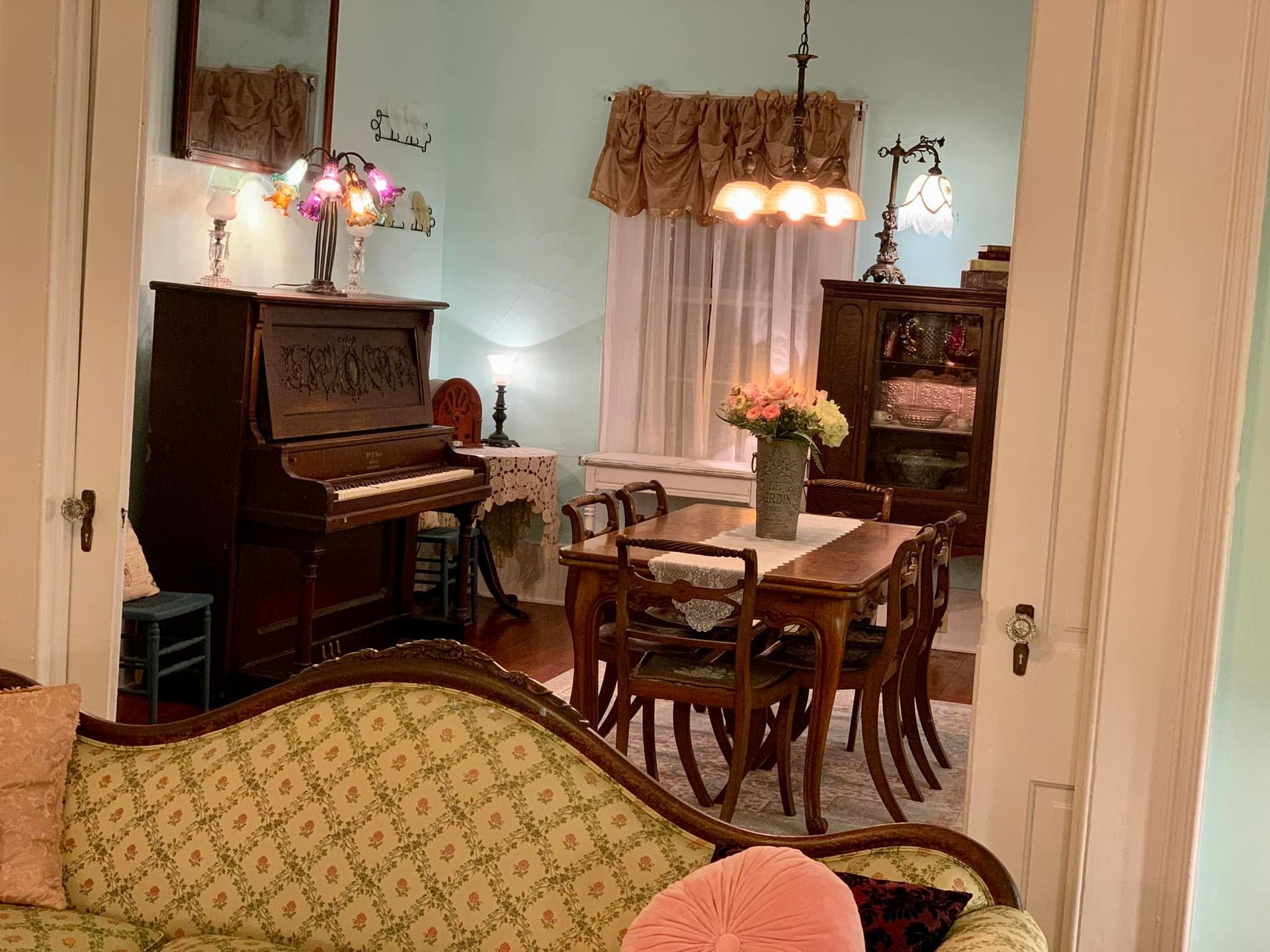A living room with a couch , piano , table and chairs.