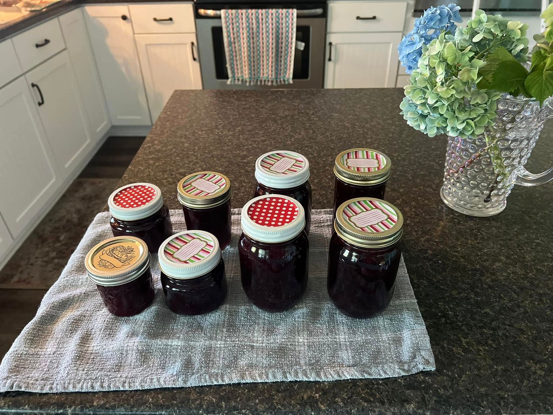 Several jars of jam are sitting on a towel on a kitchen counter.