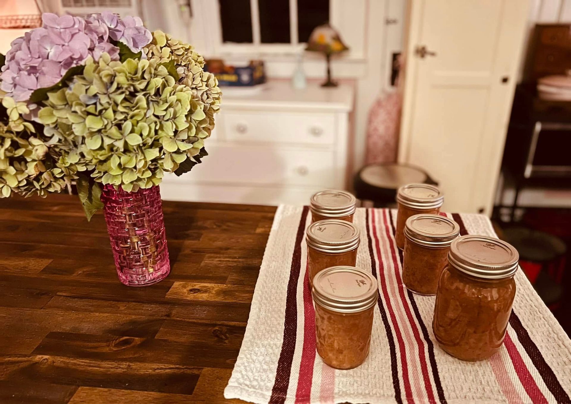 Jars of jam are sitting on a table next to a vase of flowers.