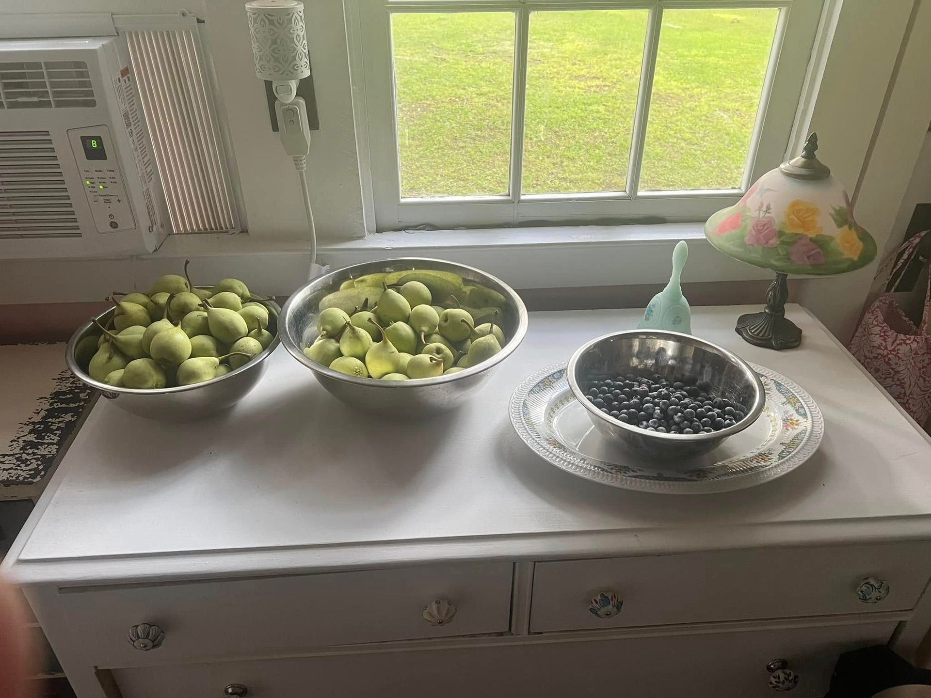 Three bowls of fruit are sitting on a white dresser in front of a window.