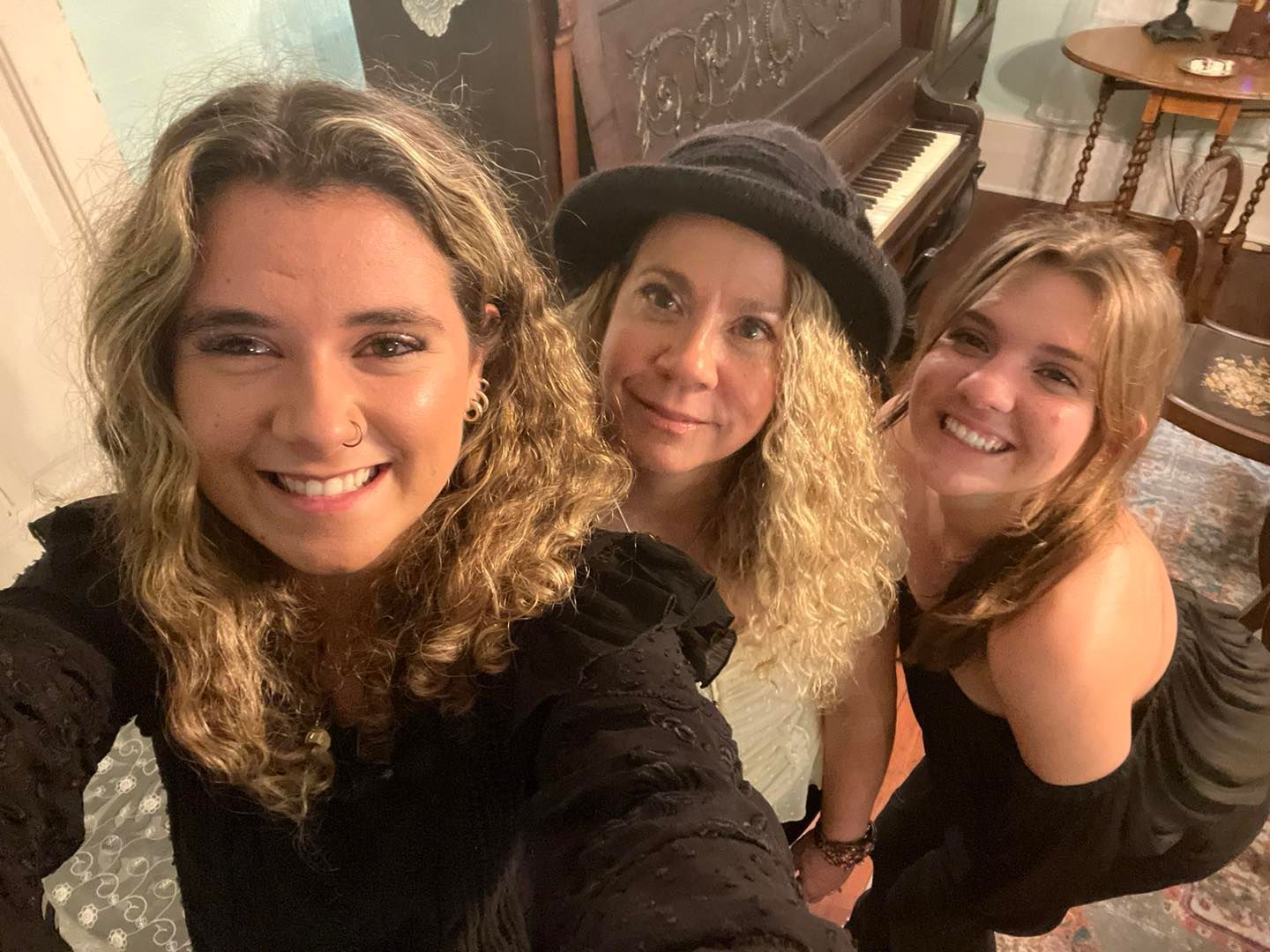 Three women are posing for a selfie in front of a piano.