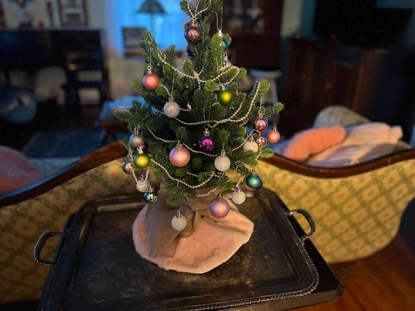 A small christmas tree is sitting on a tray in a living room.