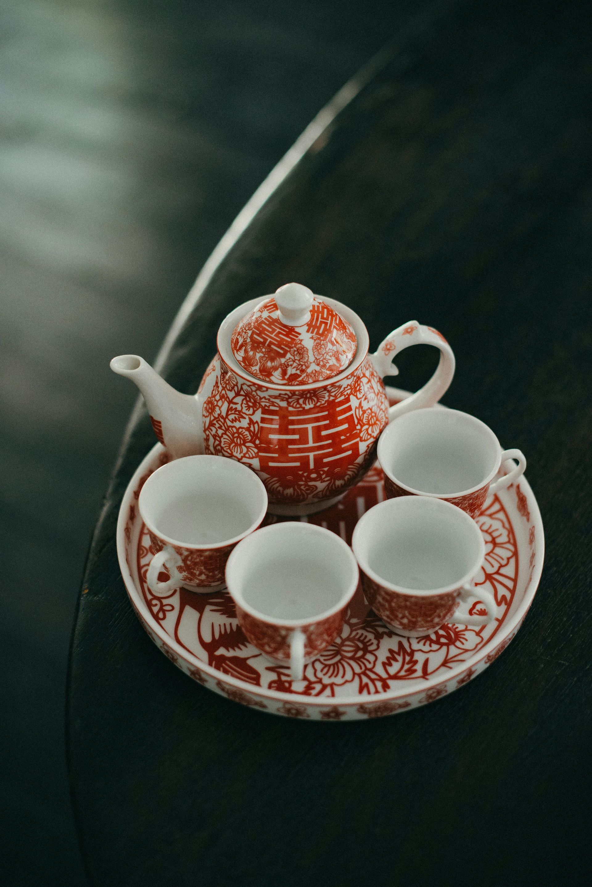A tea set with a teapot and four cups on a tray on a table.