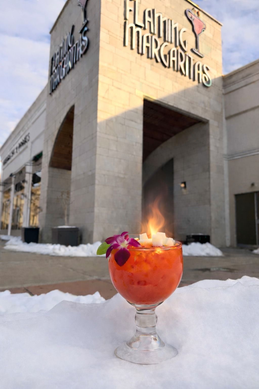 Flaming Margarita cocktail in a glass, with flames on top, in front of Flaming Margaritas restaurant, snow on ground.