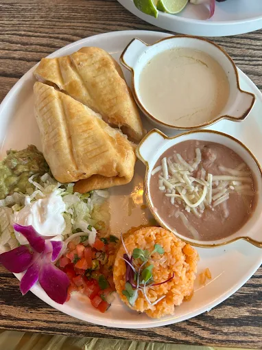 Plate with two fried burritos, dips, rice, beans, toppings, and a flower garnish.