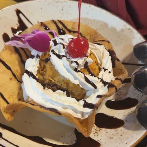 Fried ice cream dessert in a tortilla bowl, topped with whipped cream, chocolate syrup, and a cherry.
