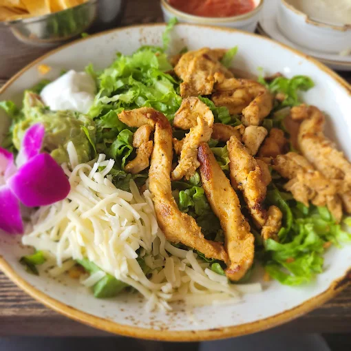 Chicken salad with lettuce, cheese, guacamole, sour cream, and a flower.
