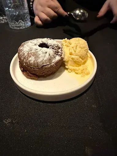 Chocolate lava cake with ice cream on a white plate, person's hands in background.
