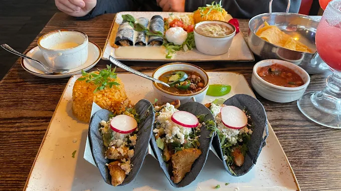 Three tacos with black shells, served with other Mexican food items.