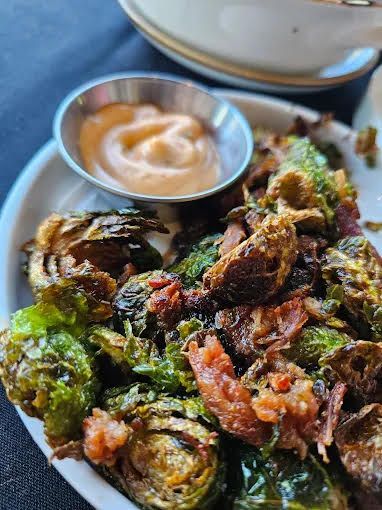 Plate of crispy fried Brussels sprouts with a small dipping sauce bowl on the side