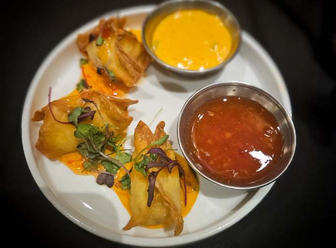 Fried dumplings with dipping sauces on a white plate.