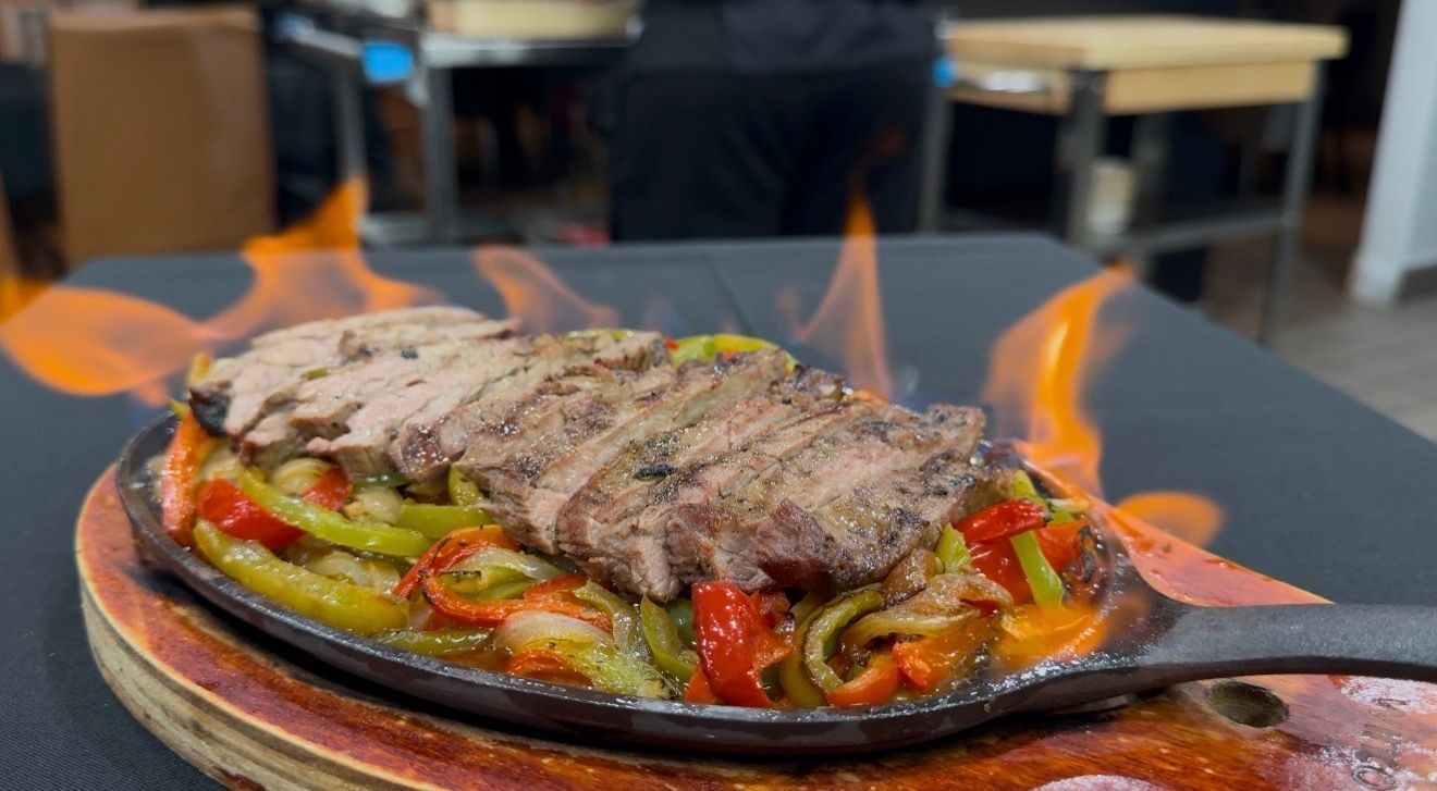 Sizzling fajitas on a cast iron skillet with flames, topped with sliced steak and colorful peppers.