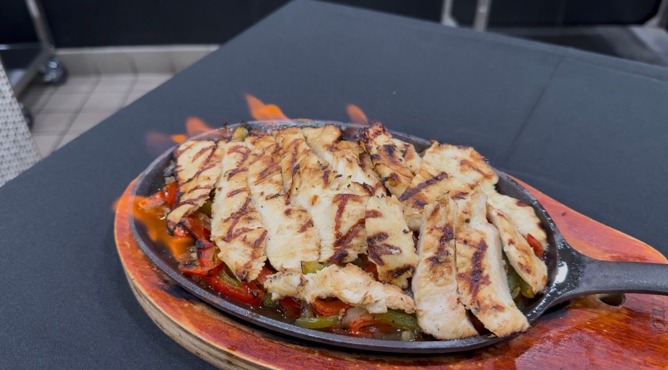 Sizzling chicken fajitas on a hot skillet with flames, served on a wooden board.