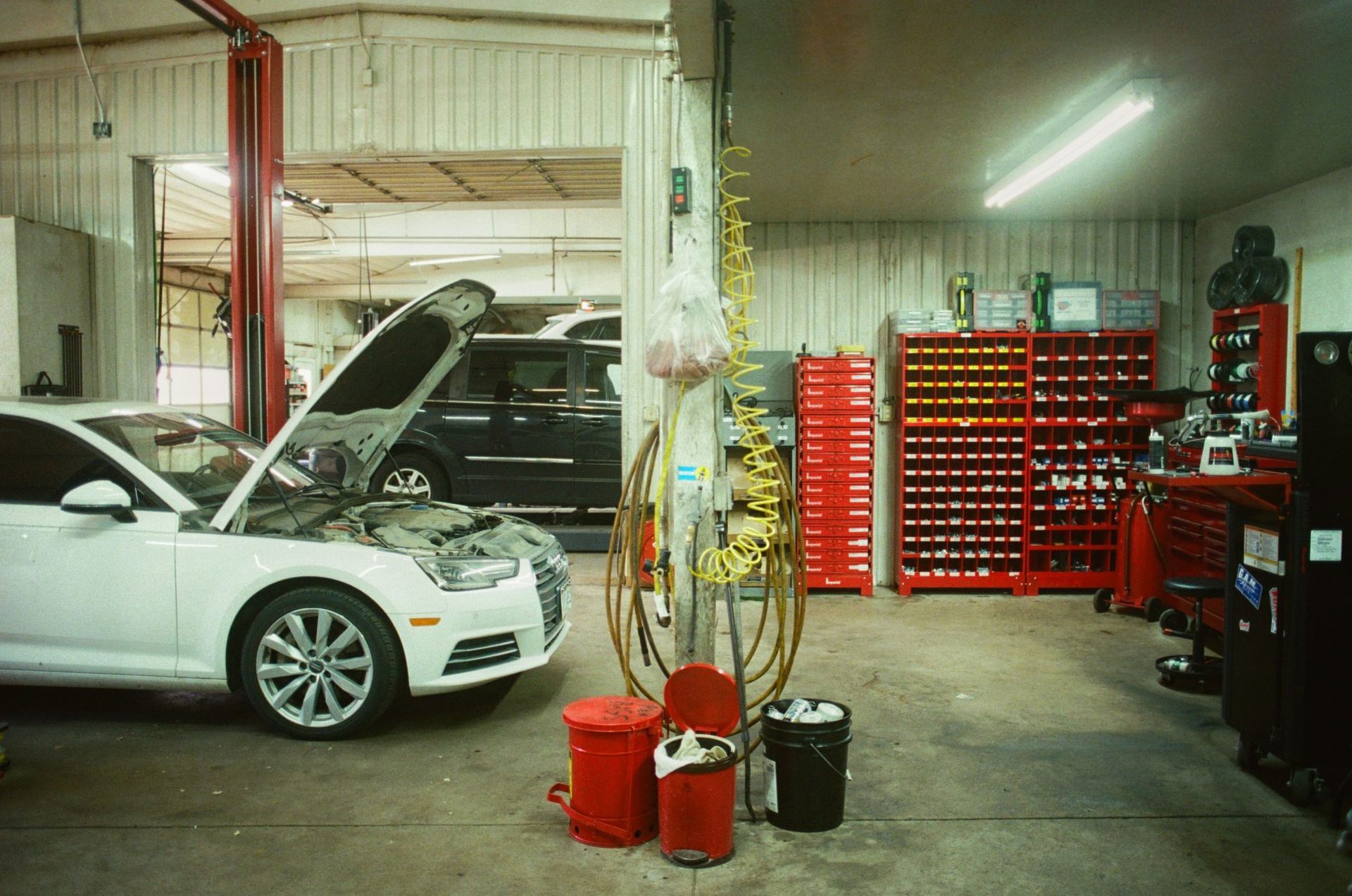 White car with hood open in an auto repair garage, surrounded by tools and red storage shelves. | Buck & Doe Auto