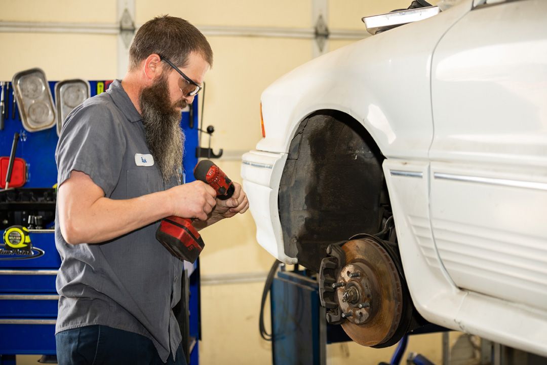Mechanic using a power tool to work on a white car lifted in a garage | Buck & Doe Auto