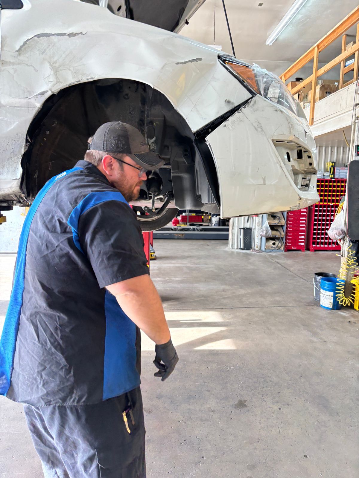 Mechanic inspecting a car’s front end in a repair shop under a raised lift | Buck & Doe Auto