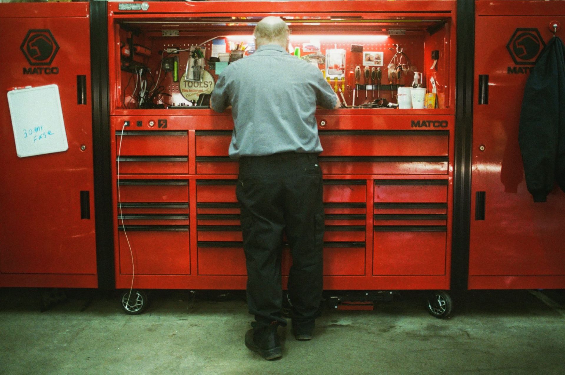 Man standing at a red tool chest in a garage workshop, facing away and working with tools. | Buck & Doe Auto