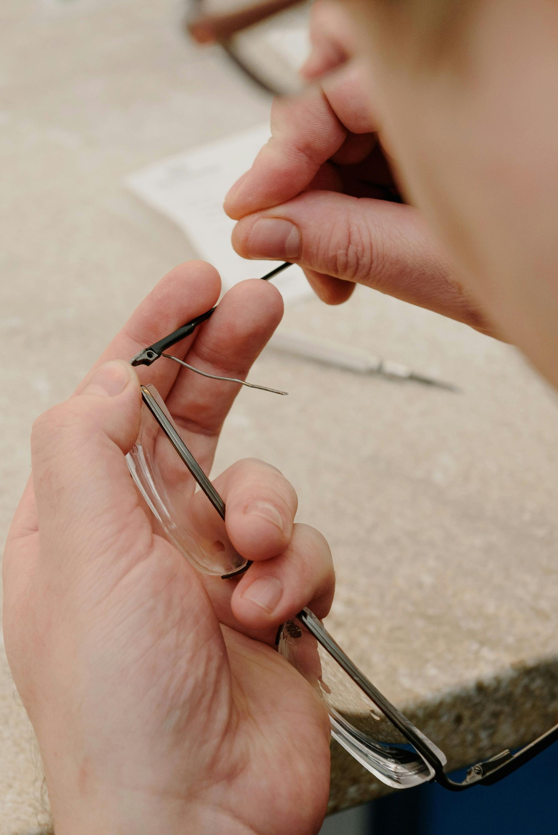 Hands holding a metal eyeglass temple, adjusting it near a tabletop.