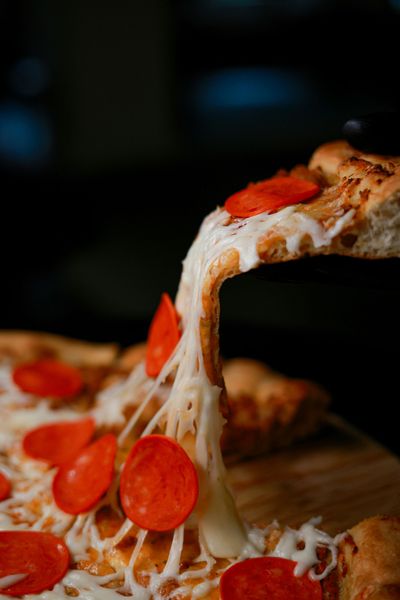 Una fetta di pizza al salame piccante e formaggio viene sollevata, con la mozzarella fusa che fuoriesce dalla pizza