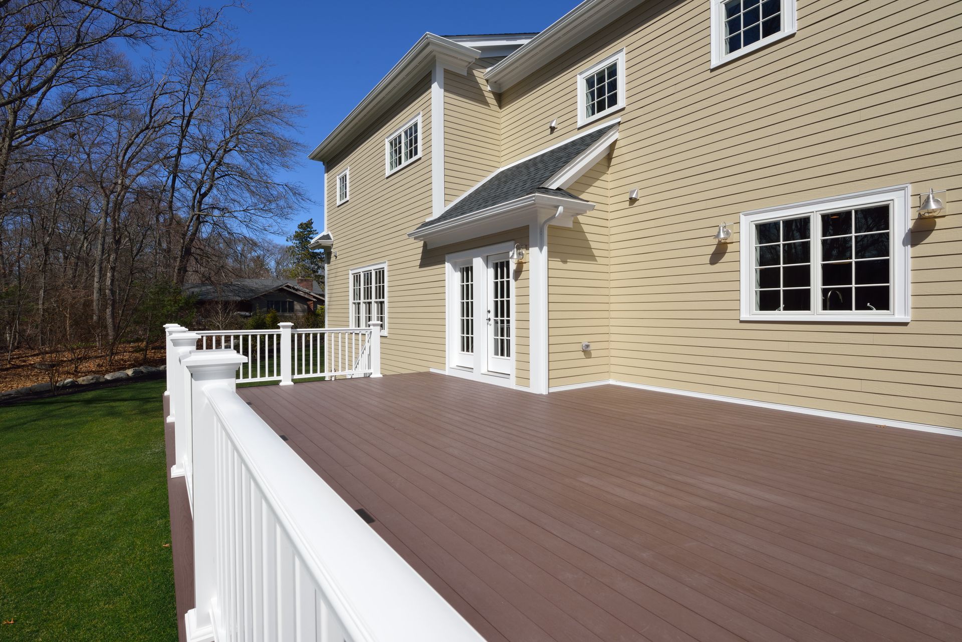A spacious backyard deck with brown composite boards and white railings, attached to a yellow house with white trim.