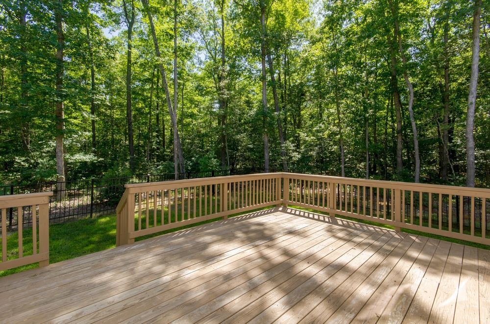 A wooden deck with a railing overlooks a lush green forest on a sunny day.