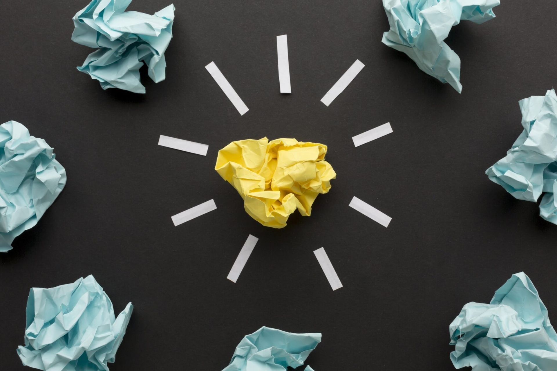 Papel amassado amarelo no centro, rodeado por papel amassado azul e linhas brancas, sobre um fundo preto.