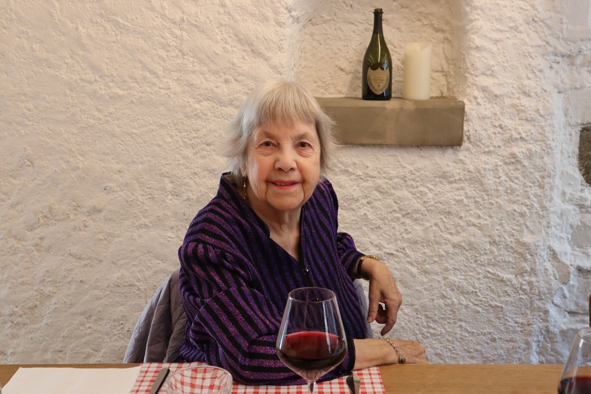 Une femme âgée est assise à une table avec un verre de vin.