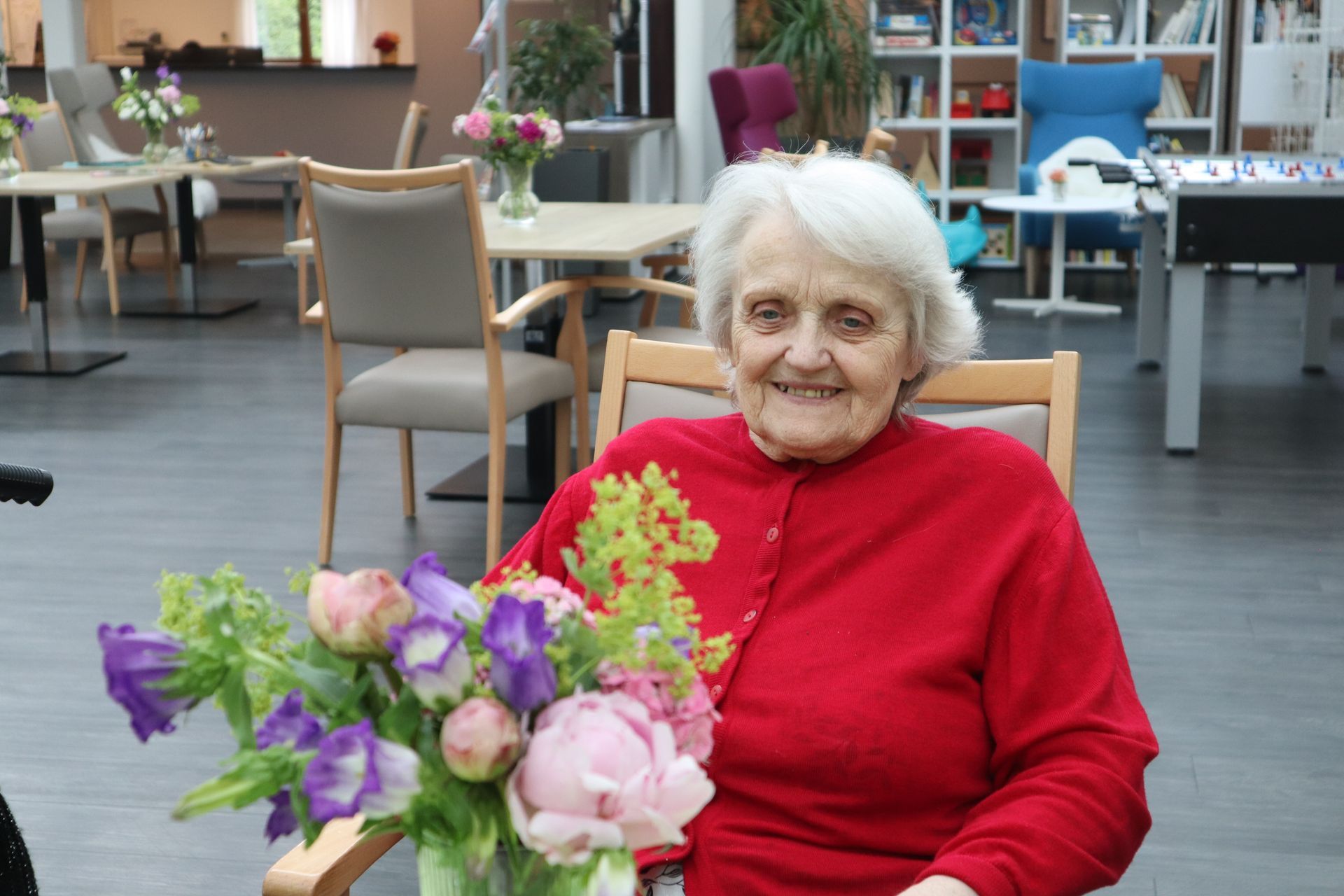 Une femme âgée est assise sur une chaise tenant un vase de fleurs.