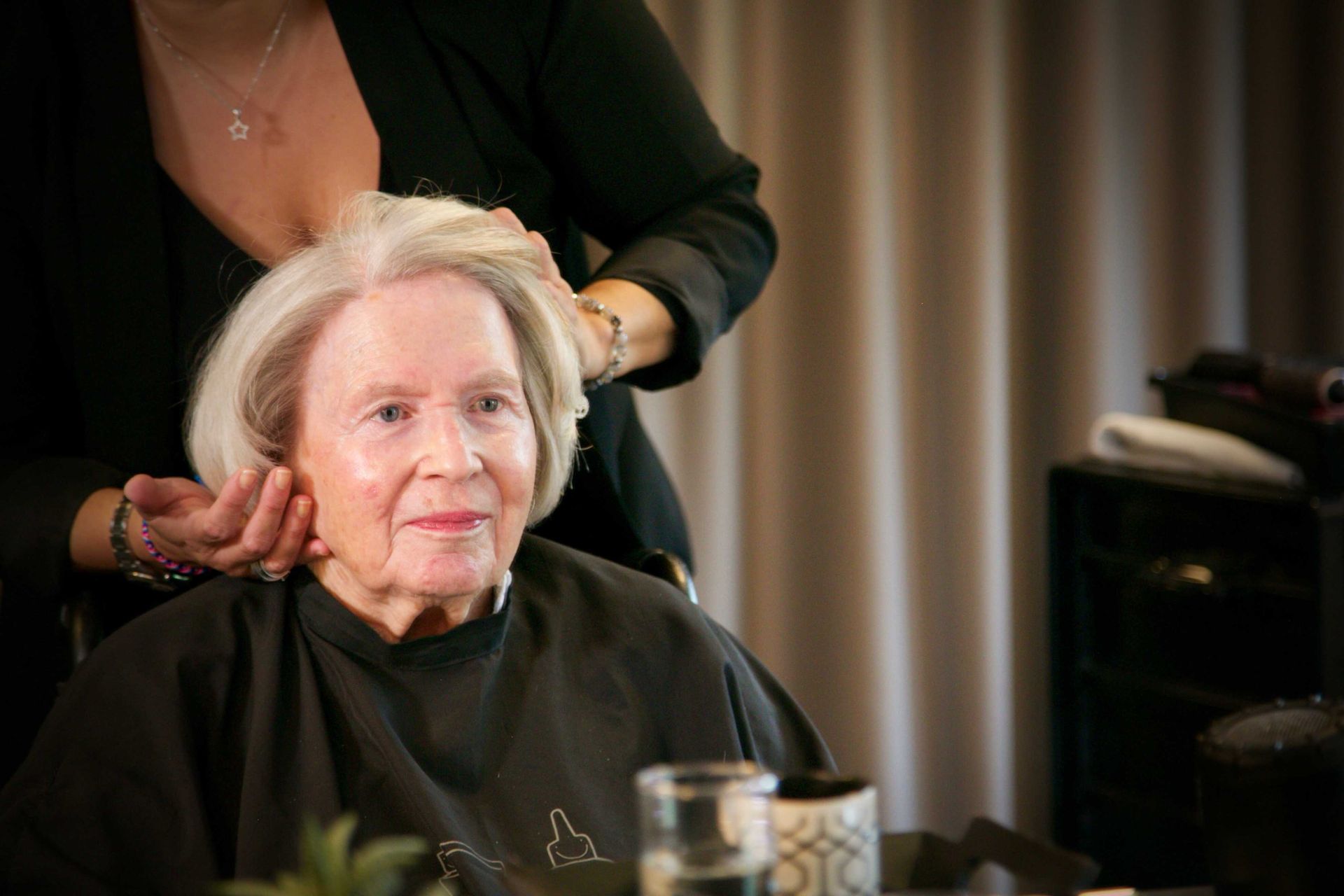Une femme âgée se fait couper les cheveux par une coiffeuse.
